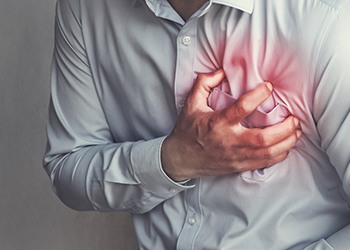 A man clutching his chest because he is experiencing a heart attack