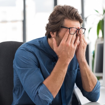Frustrated tired man sitting at desk with head in hands