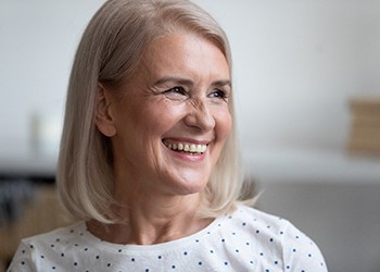 An older woman wearing a white blouse with blue polka dots and smiling while looking off to the side