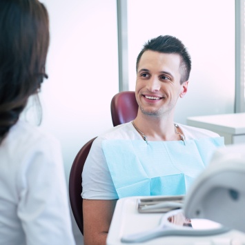 Man in dental chair smiling while talking to dental team member