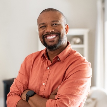 Smiling man standing in living room with arms crossed