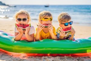 three children eating watermelon on the beach to prevent dental emergencies 