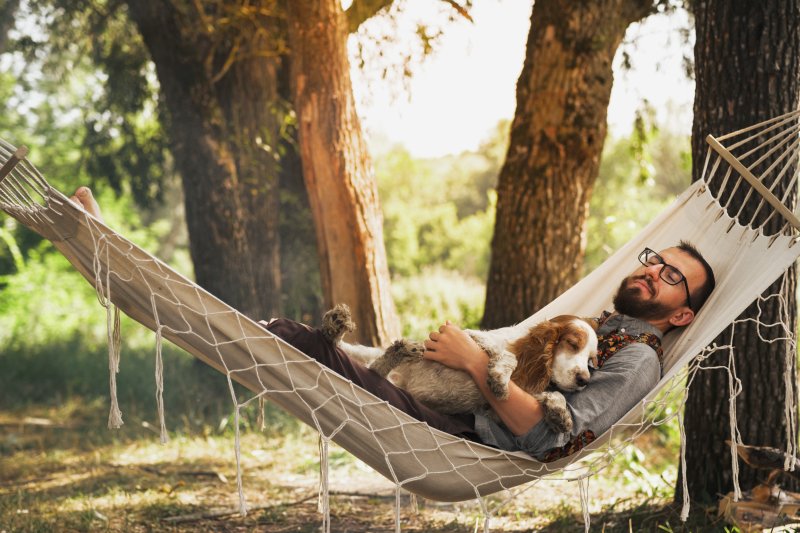 Man cuddles dog while sleeping in hammock.