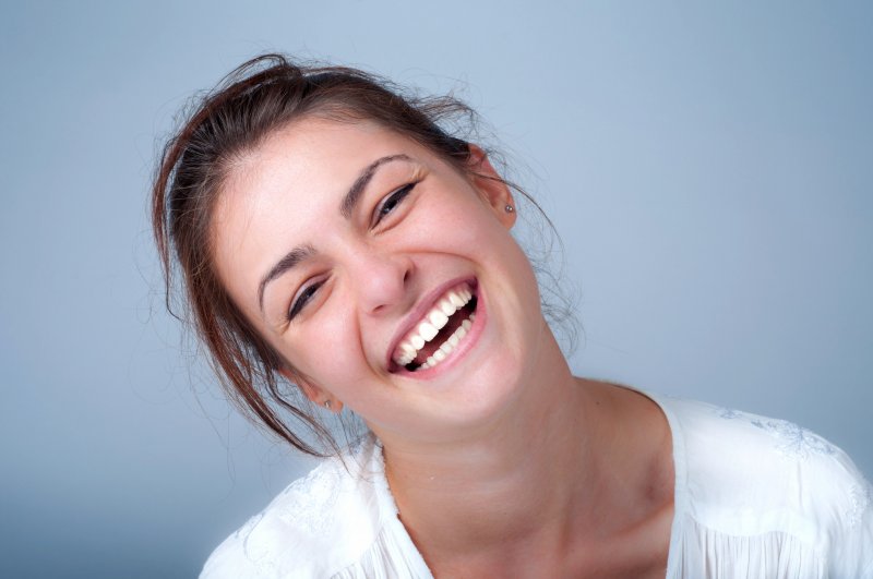 Woman tilting her head and smiling widely with bright, white teeth