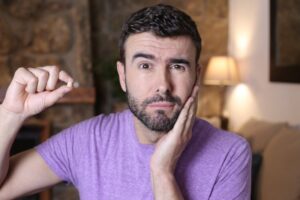 Man holding face in one hand and tooth in the other.