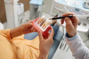 Patient holding dental implant model while dentist points to it with pen.